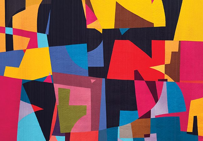 A photo of a large, irregular, brightly coloured, geometric quilt